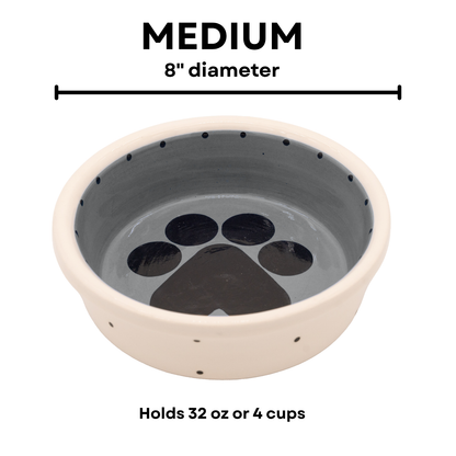Medium charcoal gray handmade ceramic dog bowl with large black paw print inside and small black dot details around the outside and inner rim, 8-inch diameter and 4-cup (32-ounce) capacity.