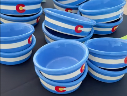 Group of blue handmade ceramic dog and cat bowls with minimalist Colorado state flag design, featuring white stripes and red C emblems with gold centers.